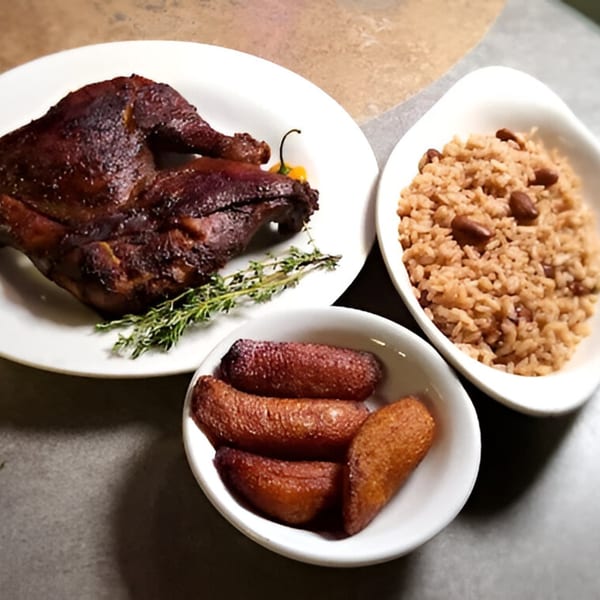 A plate of jerk chicken with thyme and a scotch bonnet pepper, alongside rice and peas and fried plantains.