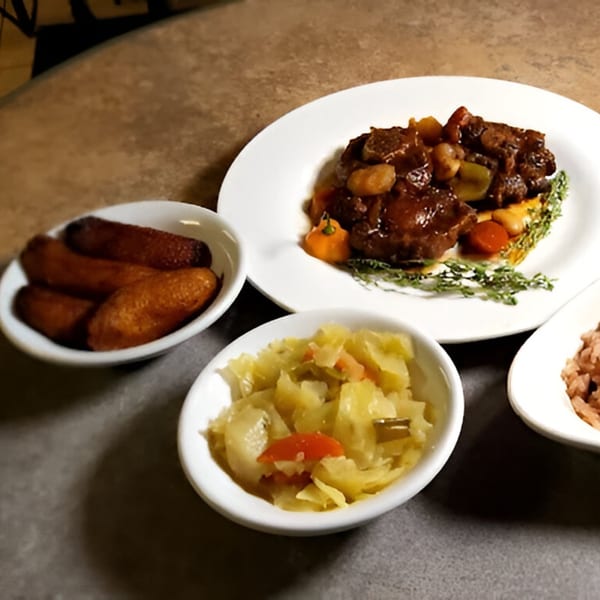 Caribbean oxtail stew with plantains, cabbage, and rice, served on a dark table.